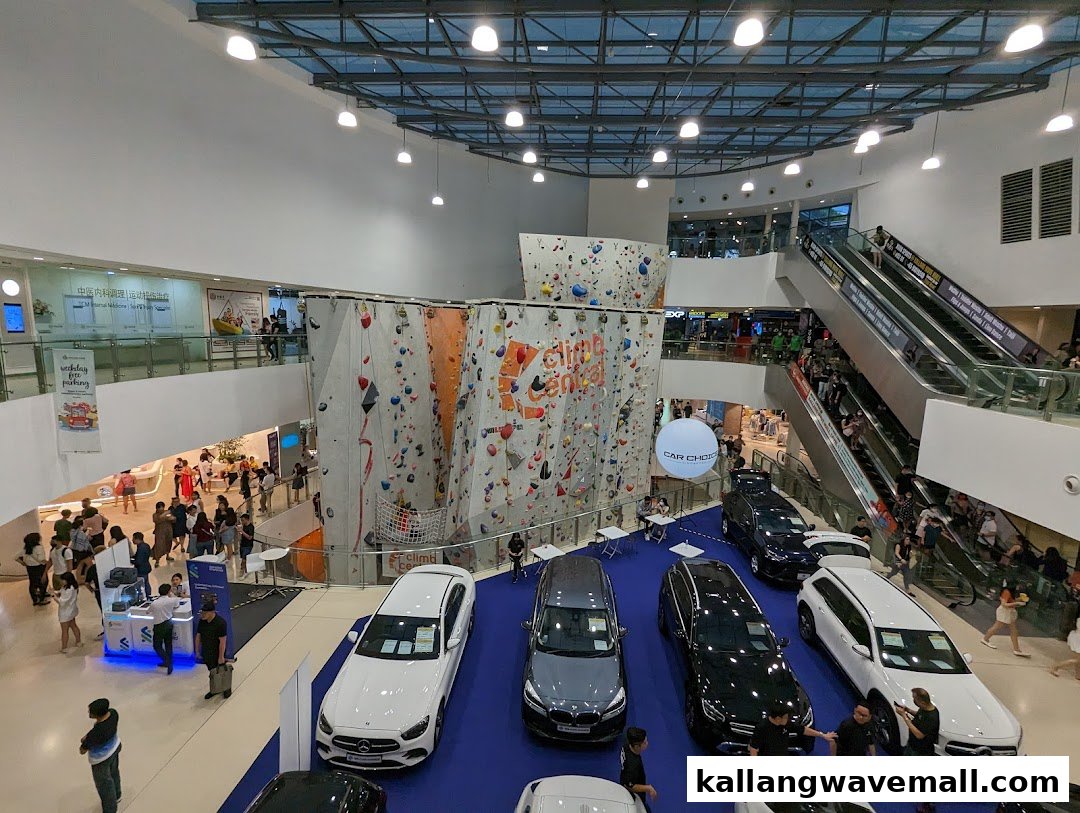 A vibrant mall interior featuring a large indoor climbing wall, a car display, and bustling shoppers.