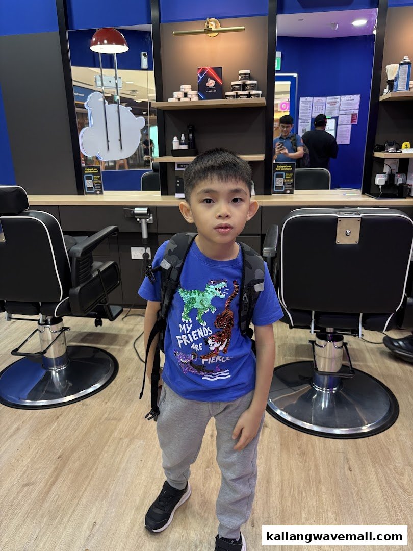 A young boy stands inside a modern barber shop with barber chairs and mirrors.