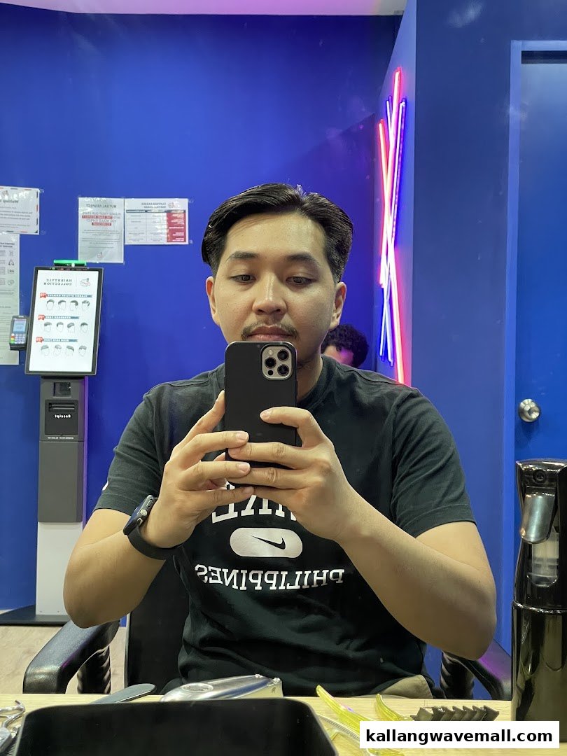 A man takes a selfie in a barbershop mirror, showcasing the vibrant blue interior.