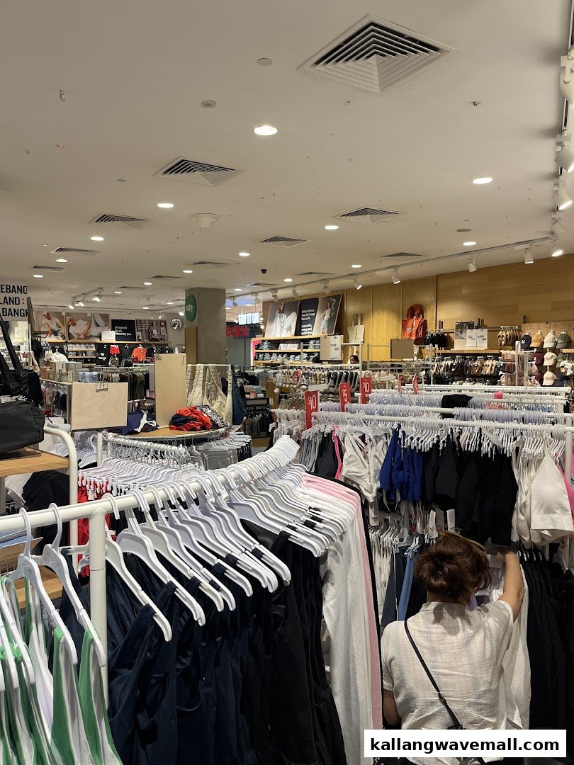 A customer browses clothing racks filled with various apparel inside a brightly lit Cotton On store.