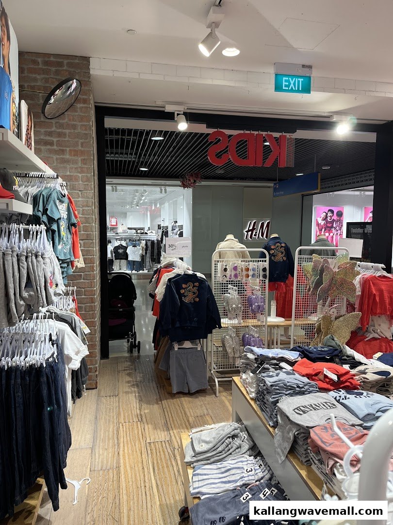 Interior view of a clothing store with racks of apparel, display tables, and a glimpse into an adjacent H&M Kids section.