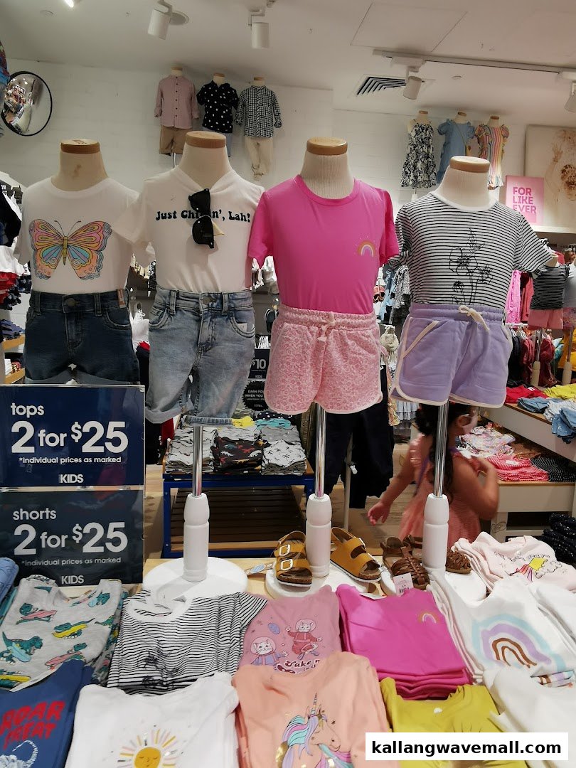 Children's clothing, including tops and shorts, displayed on mannequins and tables inside a Cotton On store.