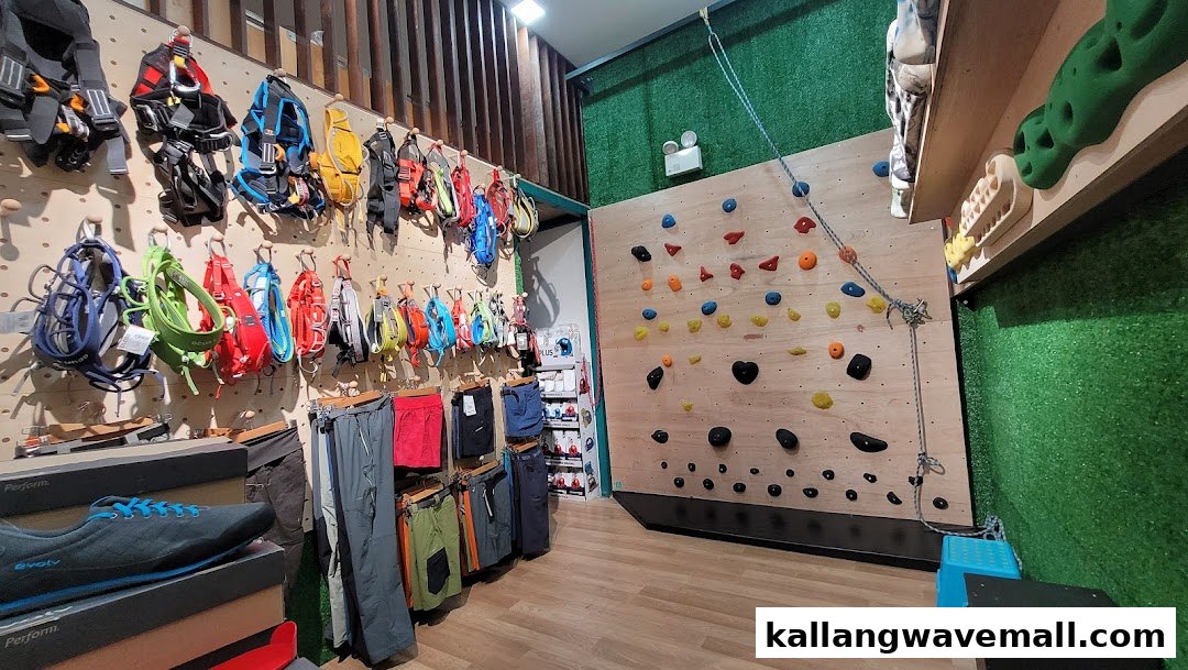 An interior view of a climbing gear shop featuring harnesses, apparel, climbing shoes, and a bouldering wall.