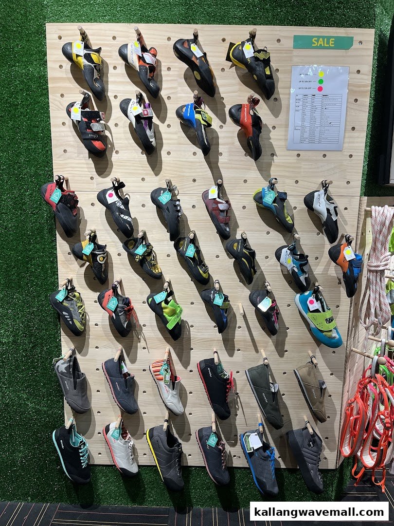 A wide selection of colorful climbing shoes displayed on a wooden pegboard in a retail store.