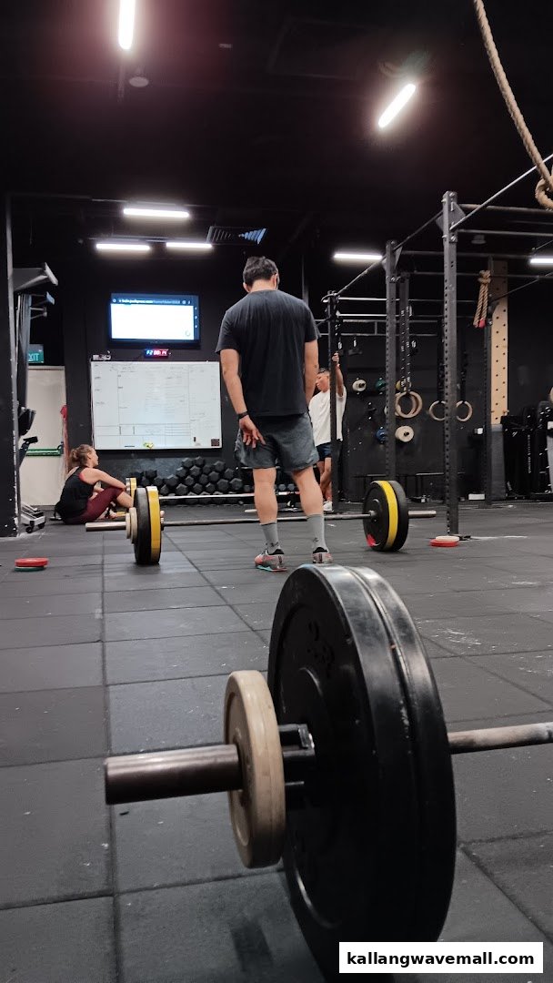 People are working out in a CrossFit gym with barbells and fitness equipment.