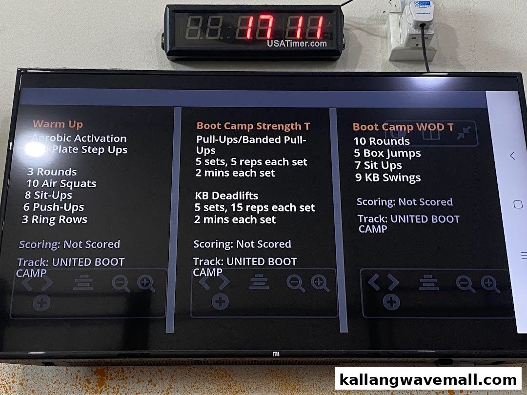 A TV screen displays the daily CrossFit workout, including warm-up, strength, and WOD details.