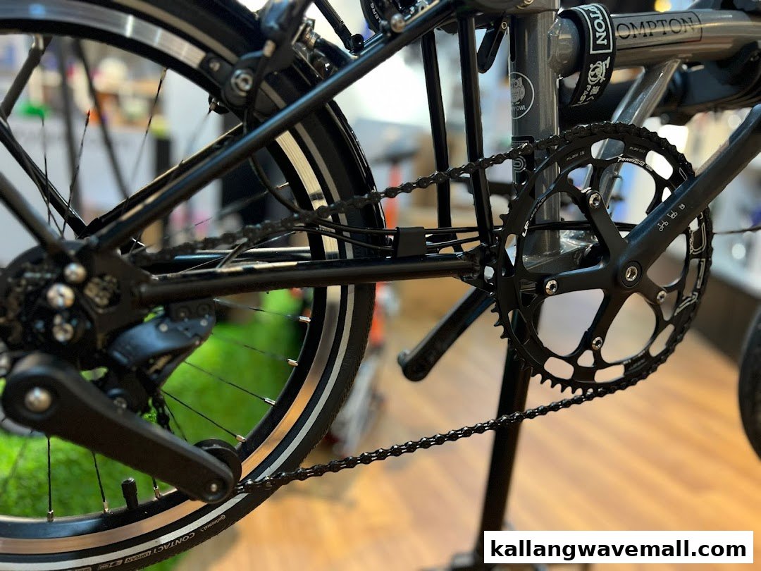 Close-up of a Brompton folding bicycle's black drivetrain, chain, and rear wheel in a shop.