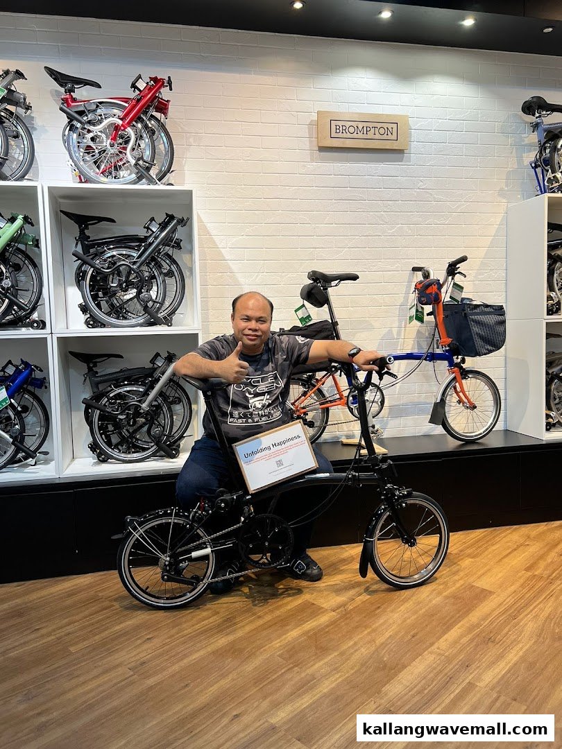 A happy customer poses with a new folding bicycle inside the CycleOxygen shop, surrounded by various models.