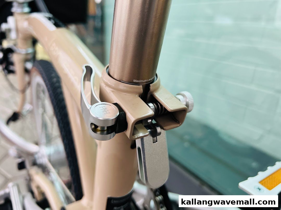 Close-up of a beige folding bicycle's seat post clamp and frame, highlighting intricate design details.