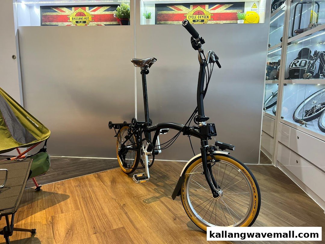A black folding bicycle displayed in a modern retail space with cycling accessories and a camping chair.