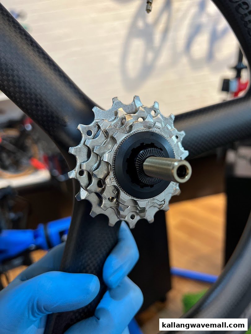Close-up of a bicycle cassette being installed or serviced on a carbon fiber wheel by a gloved hand.