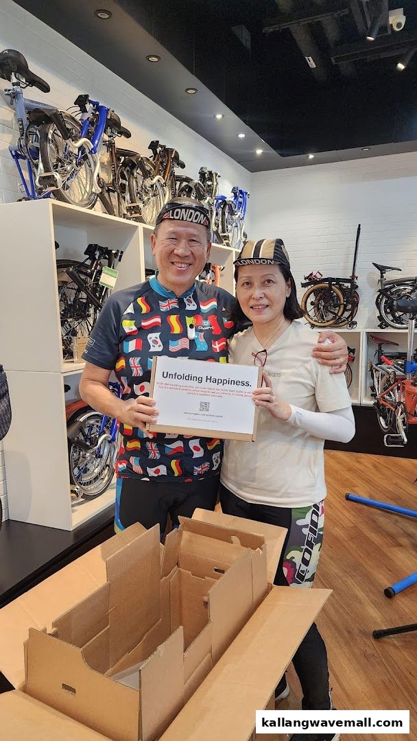 Two smiling customers hold a box labeled 'Unfolding Happiness' inside a bicycle shop filled with folding bikes.