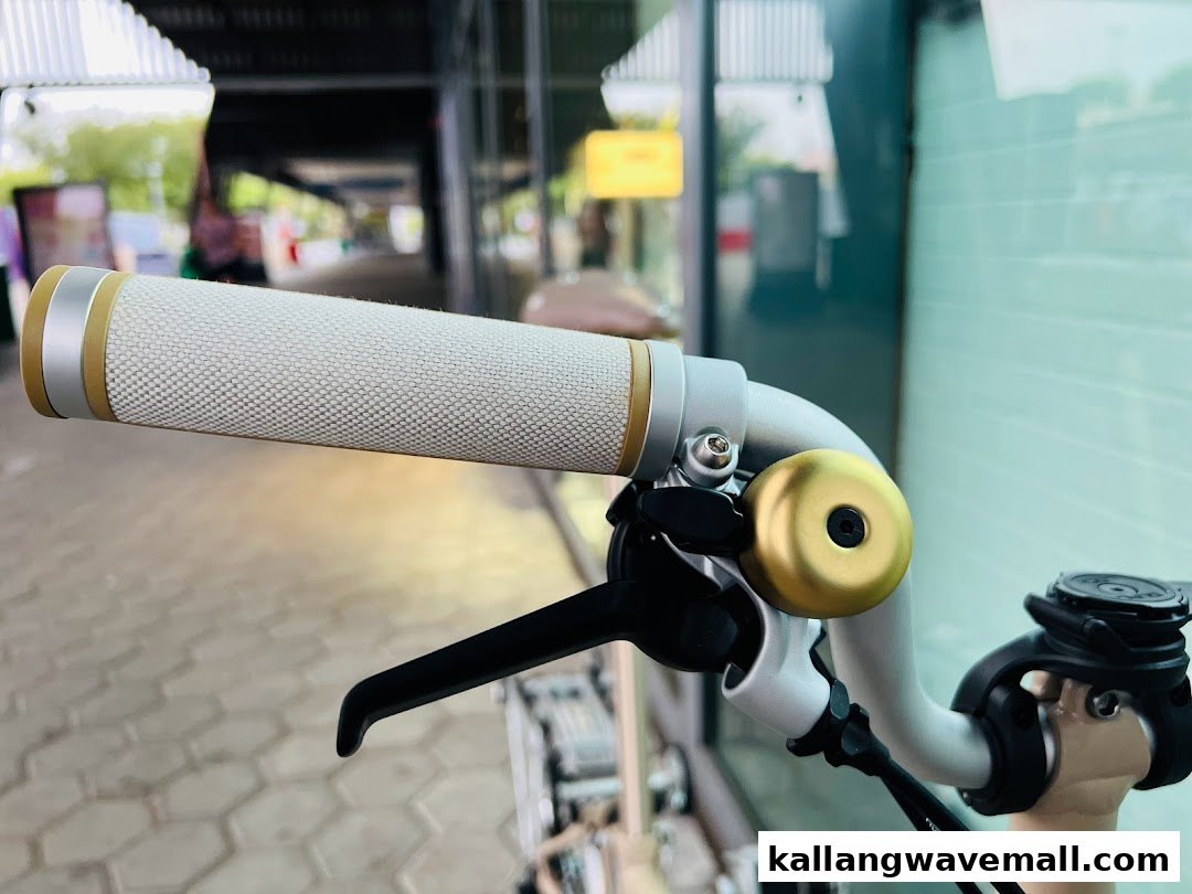 Close-up of a bicycle handlebar featuring a textured grip and a golden bell, showcasing cycling accessory detail.