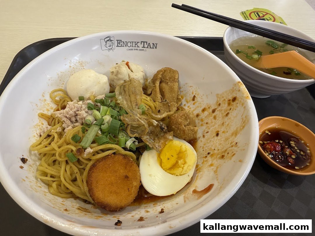 A close-up of a delicious bowl of Encik Tan's signature noodles with various toppings and a side of soup.