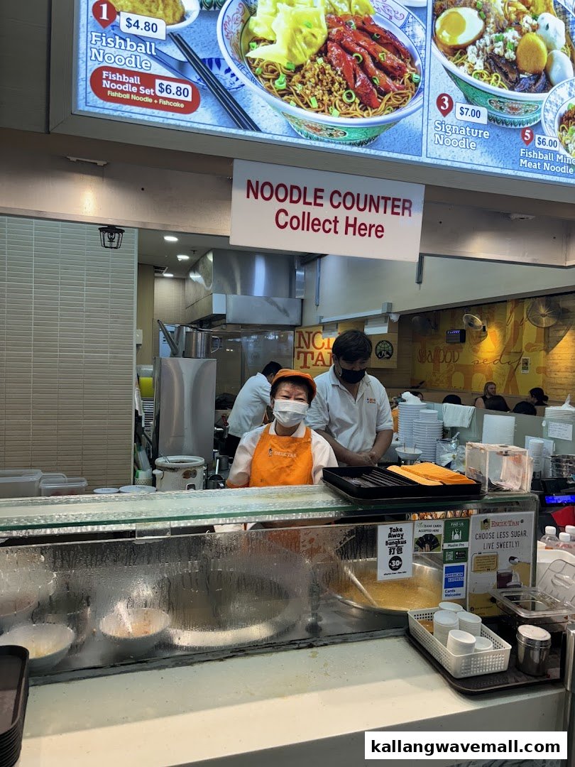 Staff preparing food at Encik Tan's noodle counter with a menu board visible above.