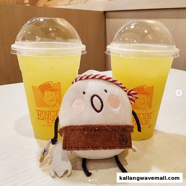 Two yellow drinks from Encik Tan with a cute plush mascot on a table.
