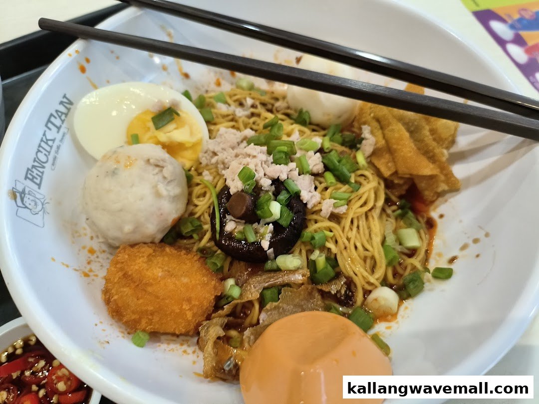 A close-up of a hearty bowl of Encik Tan's signature noodles with various toppings and chopsticks.