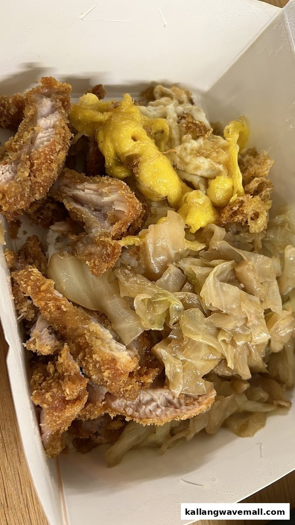 A close-up of a takeaway meal featuring crispy fried chicken, scrambled eggs, and braised cabbage over rice.