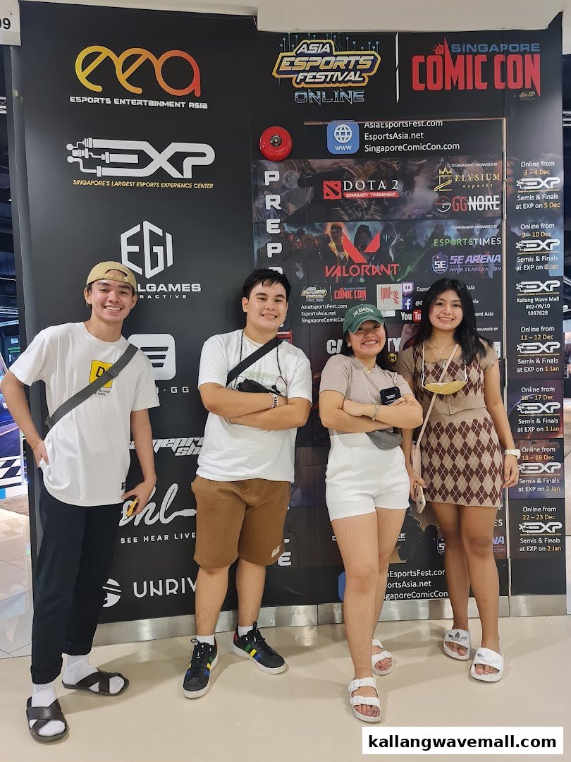 Four young people pose in front of a large promotional banner for an esports festival and experience center.