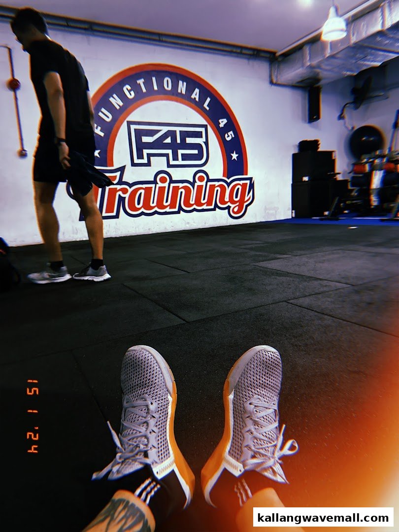 A person's feet in athletic shoes on a gym floor, with the F45 Training logo visible on the wall.