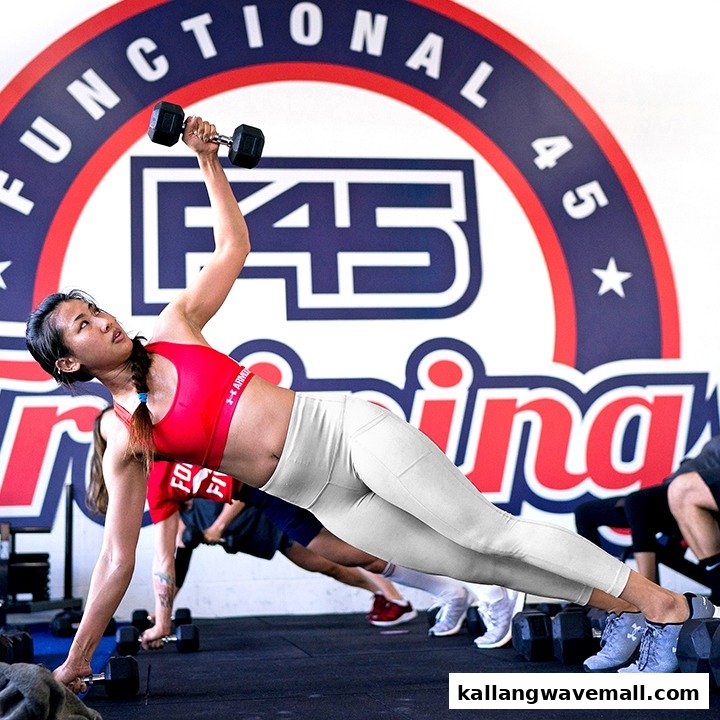 A woman performs a side plank with a dumbbell during a functional training session at F45 Training.