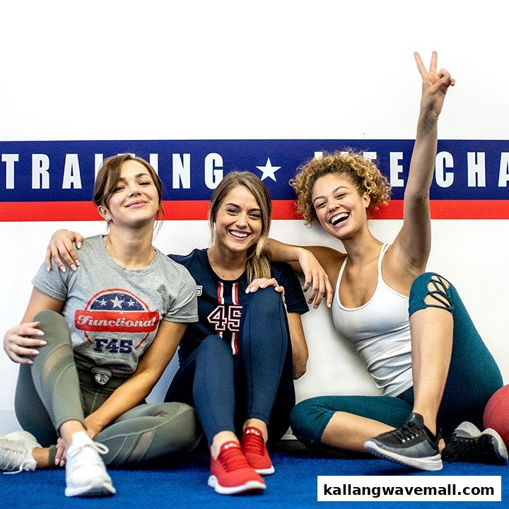Three smiling women in activewear sitting on a blue mat in an F45 Training gym.