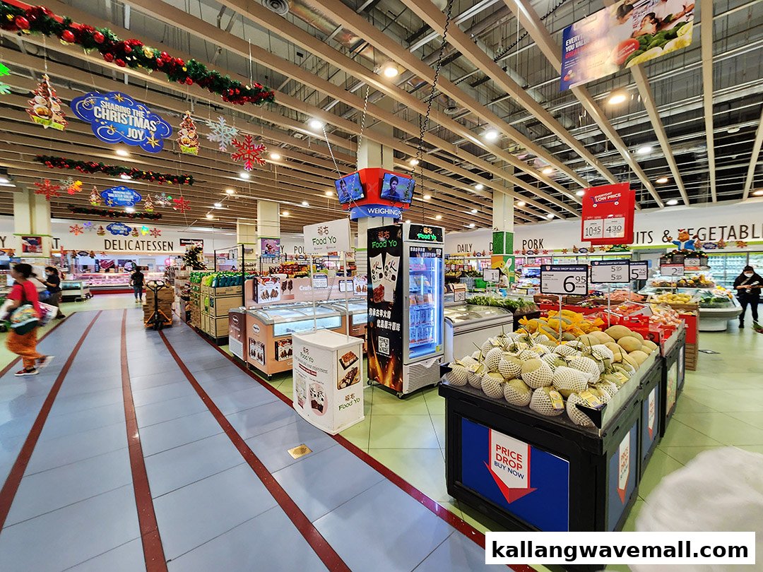 Interior view of a supermarket aisle with fresh produce, deli section, and festive Christmas decorations.