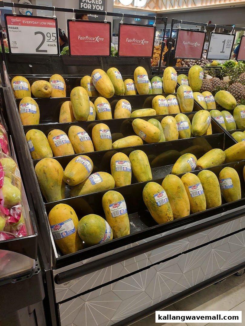 A vibrant display of fresh papayas and other fruits in a FairPrice Xtra supermarket aisle.