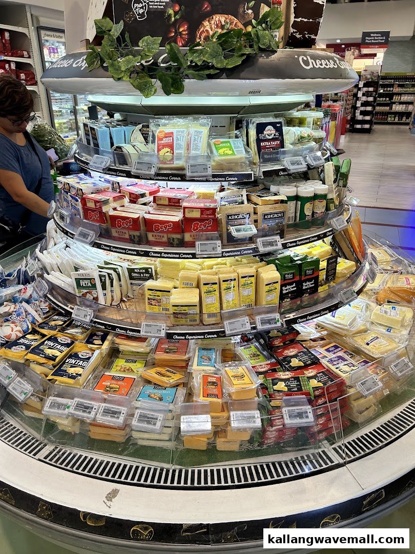 A large, circular refrigerated display showcasing a wide variety of cheeses at FairPrice Xtra.