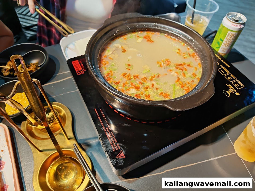A bubbling hotpot on an induction cooker, surrounded by drinks and golden utensils, ready for a delicious meal.