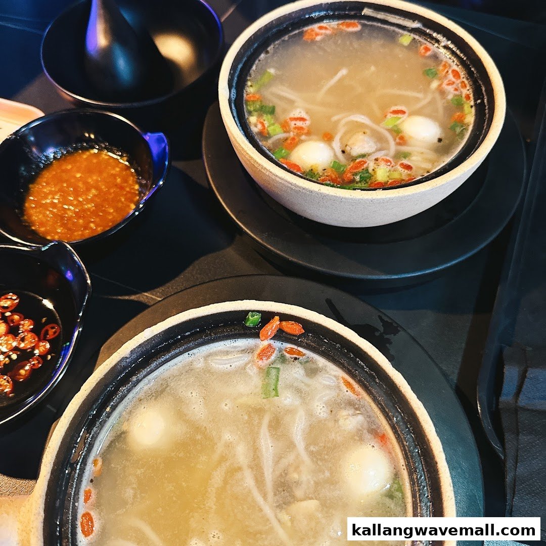 Two steaming bowls of hotpot with various ingredients and dipping sauces on a dark table.