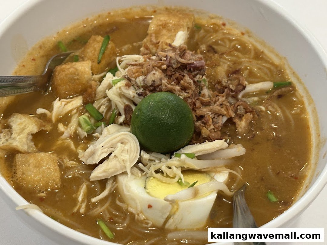 A close-up of a delicious bowl of curry noodles with shredded chicken, tofu, egg, and lime.
