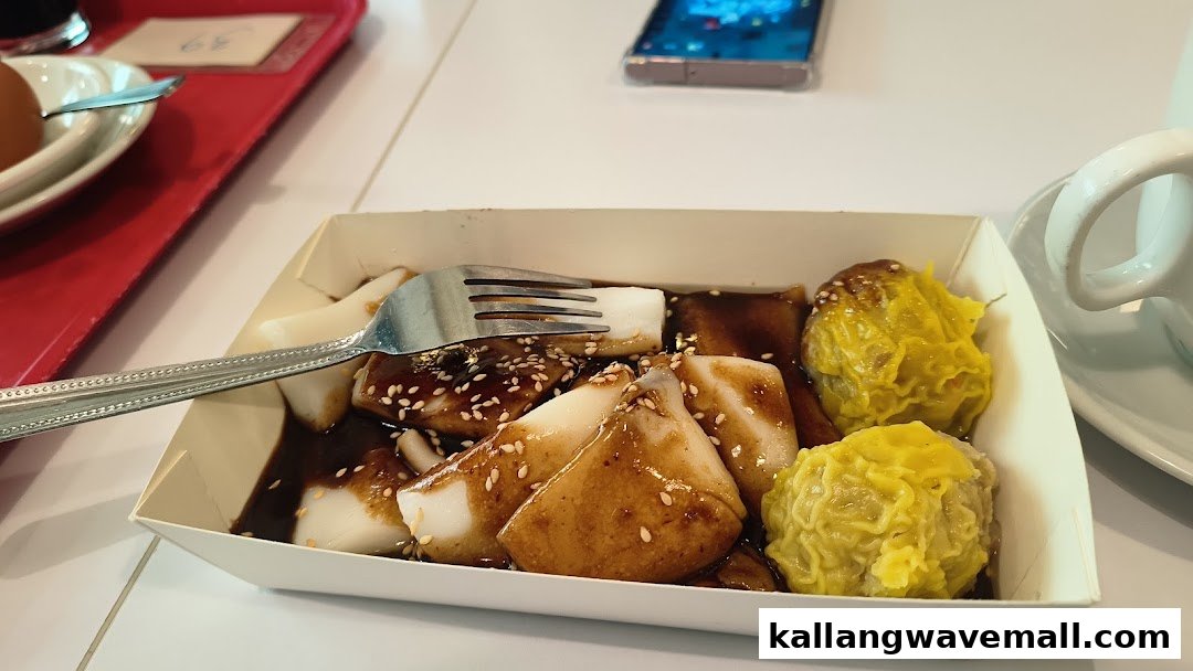A close-up of rice rolls (Chee Cheong Fun) and siew mai in a paper tray on a table.