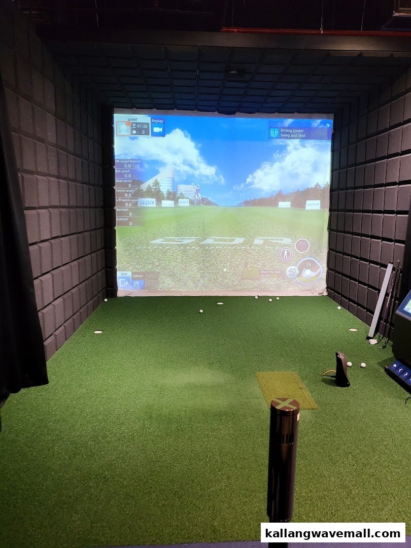 An indoor golf simulator bay with a large screen displaying a virtual golf course.