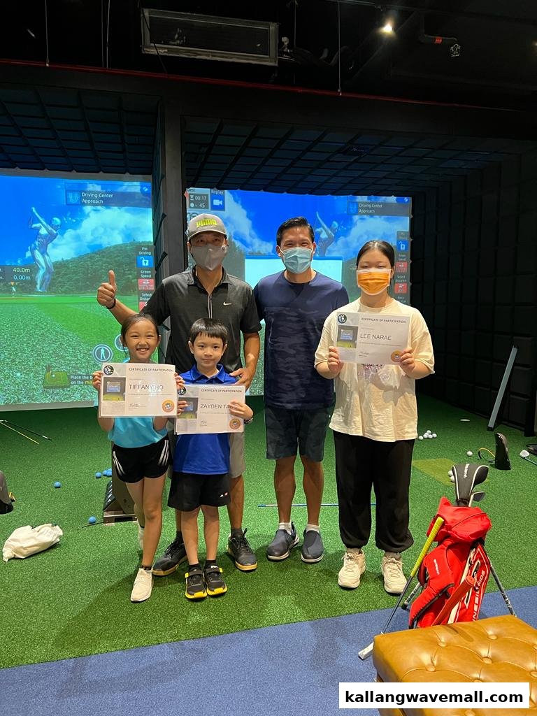 A group of adults and children holding certificates in an indoor golf simulator setting.