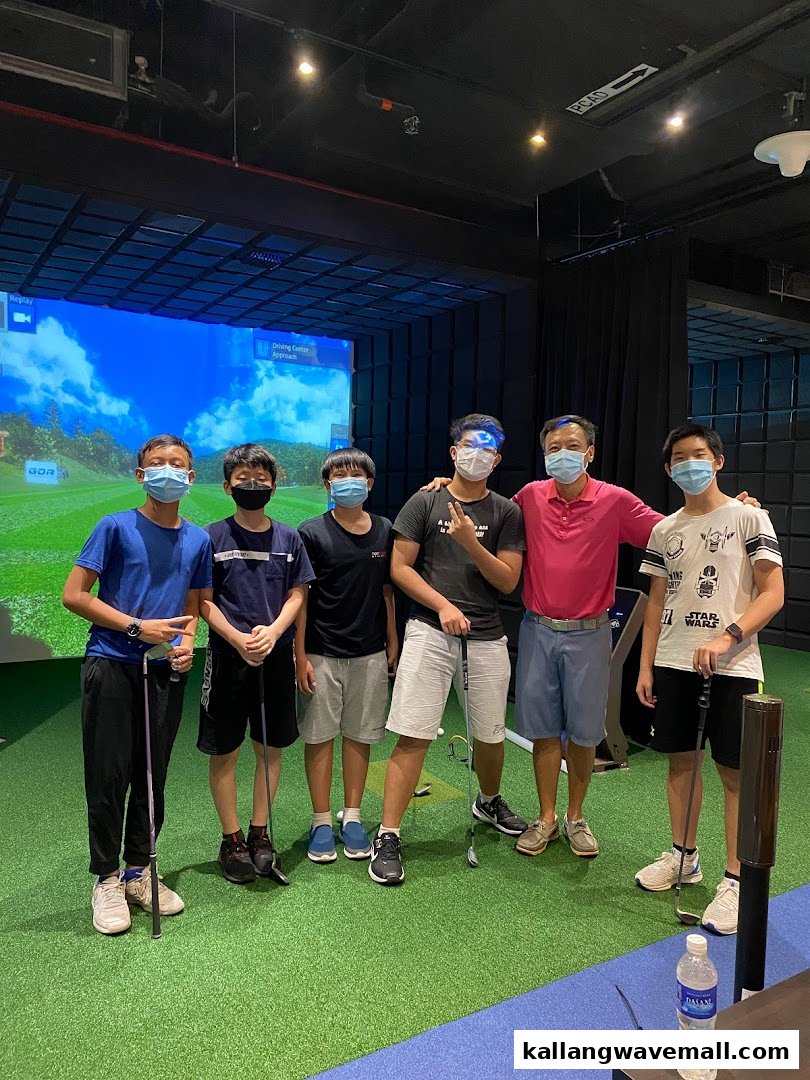 A group of people, including adults and children, posing with golf clubs in an indoor golf simulator.