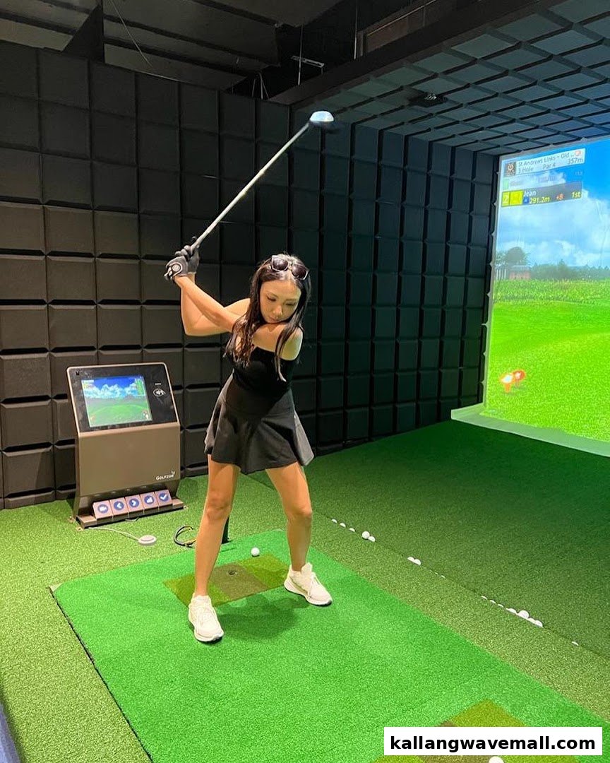 A woman in a black outfit swings a golf club in an indoor golf simulator at Golfwav.
