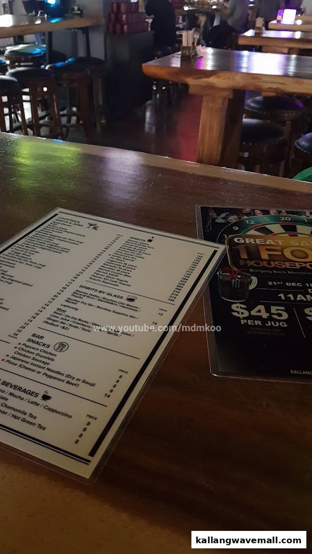 A menu and a promotional flyer on a wooden bar counter inside a dimly lit bar or restaurant.