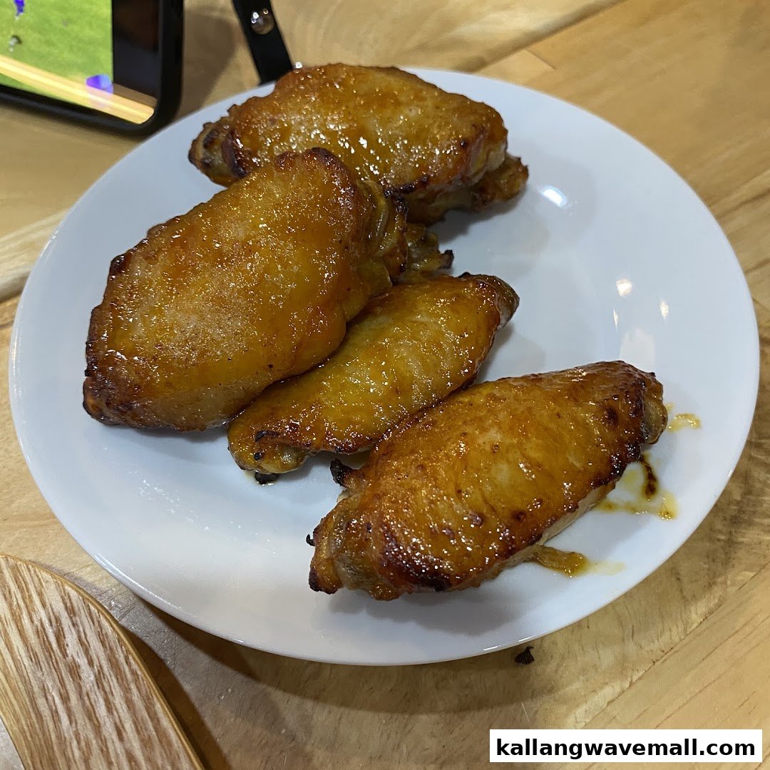 A plate of four golden-brown, glazed chicken wings on a white plate.