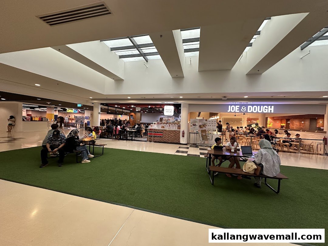 A spacious mall food court with various eateries, including a pizza shop, and people dining.