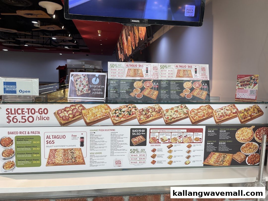 An interior view of Gourmet Pizza To Go! showcasing various pizza slices, baked rice, pasta, and menu boards.
