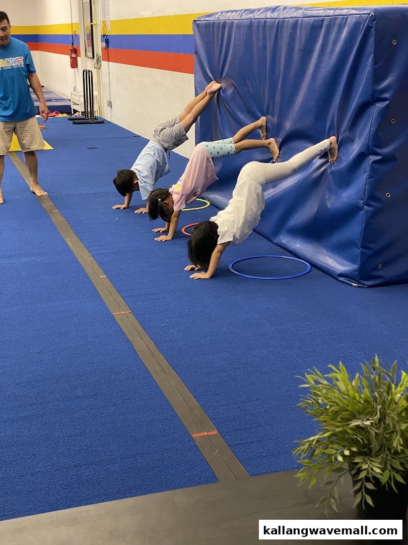 Children practice handstands against a padded wall with an instructor at GymKraft.