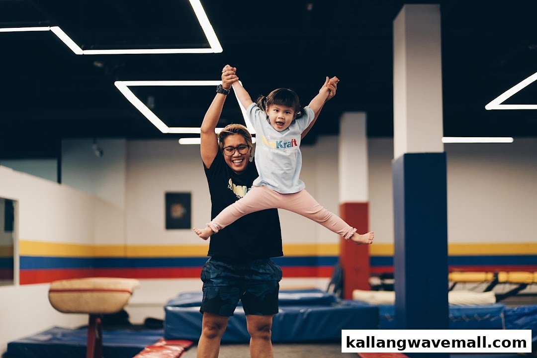 An adult holds a child who is joyfully jumping in a vibrant gym environment.