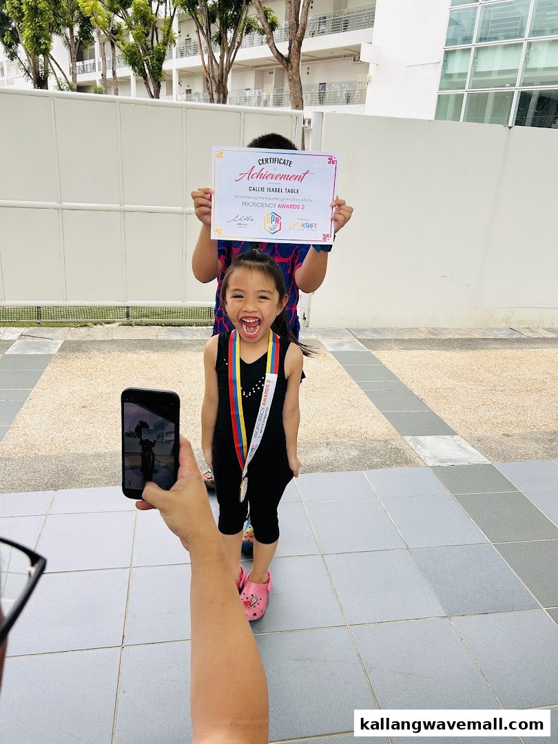 A child proudly displays a medal and certificate from GymKraft, while being photographed.