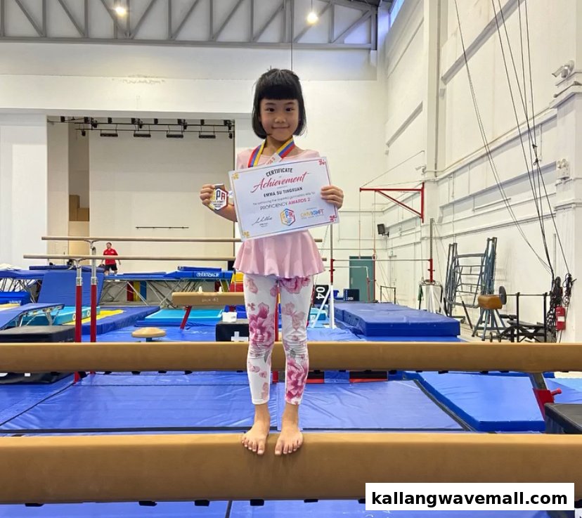 A young girl proudly displays her gymnastics achievement certificate and medal on a balance beam at GymKraft.