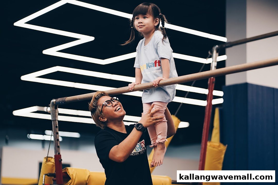 An instructor helps a young child on a gymnastics bar at GymKraft, fostering fun and skill development.