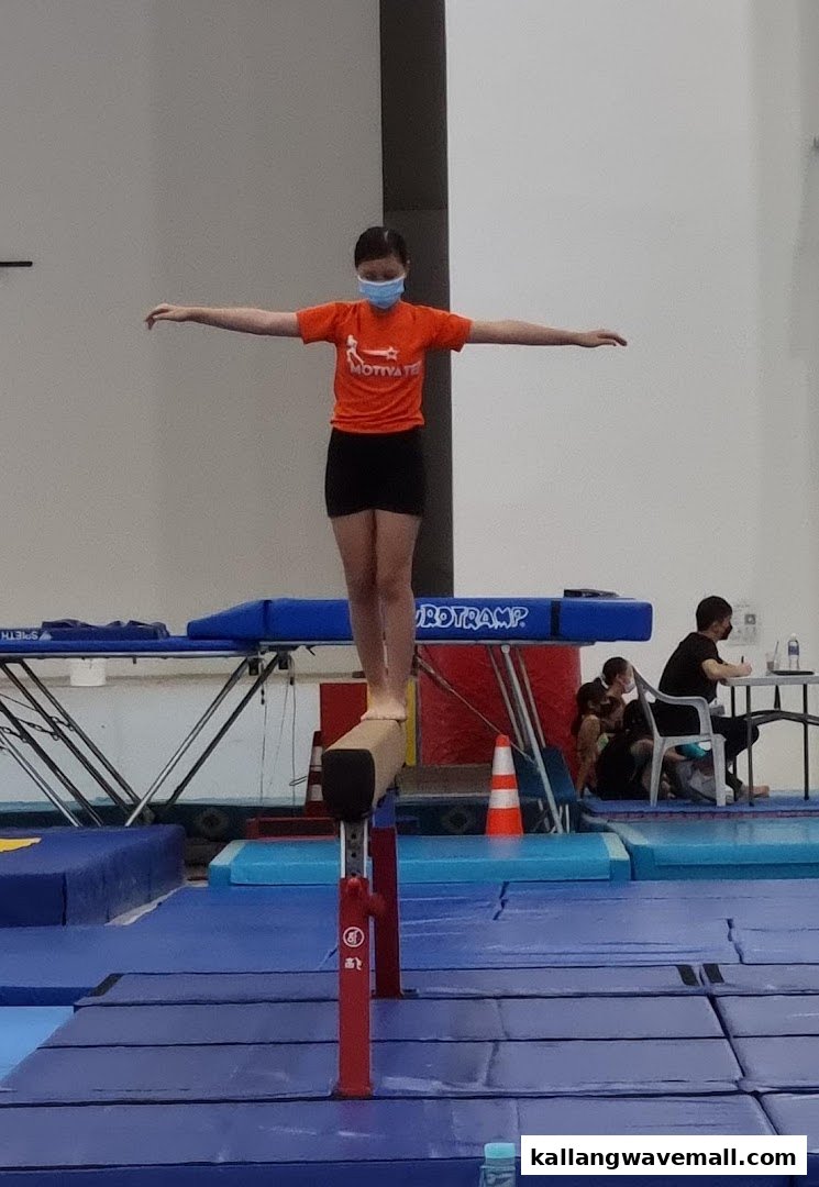 A young person in an orange shirt balancing on a gymnastics beam at GymKraft.