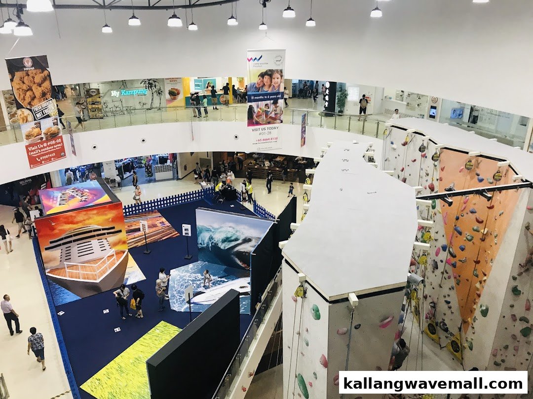 An aerial view of a vibrant multi-level shopping mall interior featuring a climbing wall and diverse retail spaces.