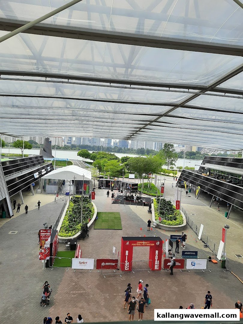 An aerial view of an outdoor plaza with people, event booths, and a lake/cityscape backdrop under a large canopy.
