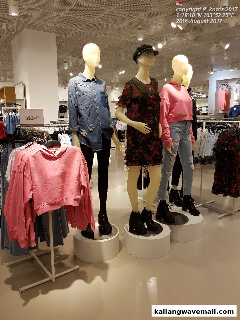 Mannequins display trendy clothing, including denim, floral dresses, and pink hoodies, inside a vibrant retail store.